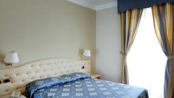 Una camera d'albergo con un letto grande, due comodini, un telefono e una finestra con tende.