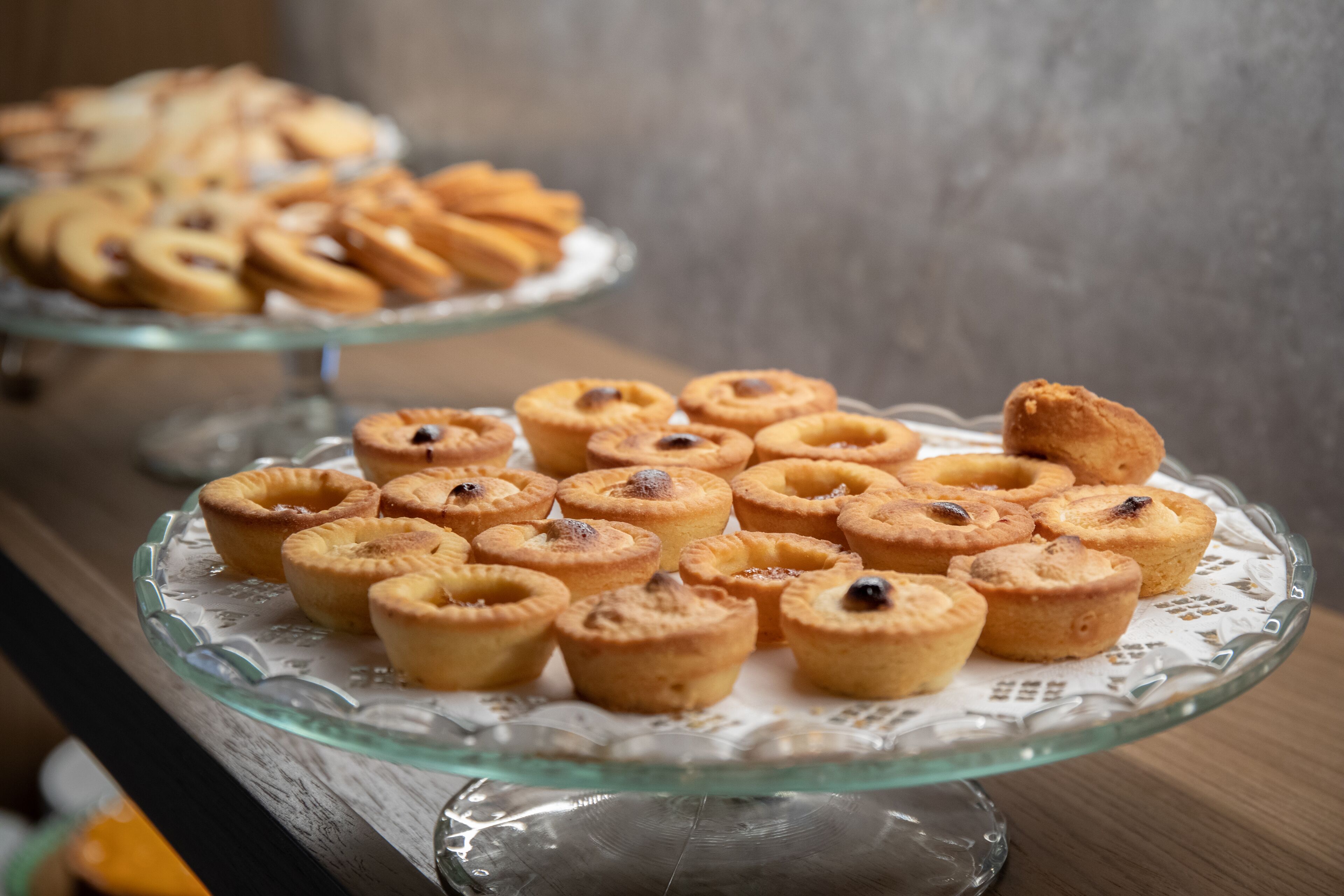 A glass display case with various baked goods, including mini pies and tarts, on a wooden surface.