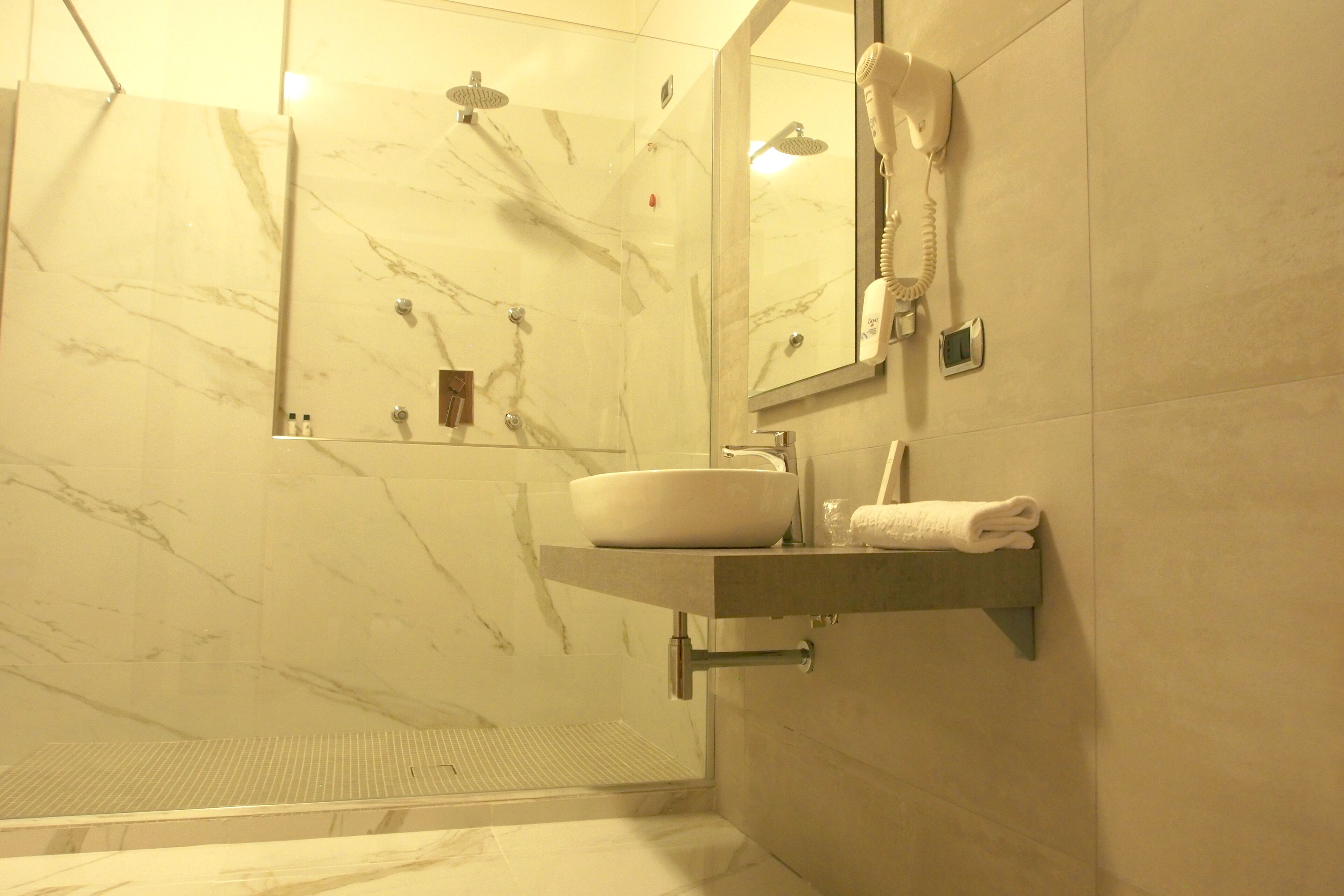 A bathroom with a marble sink, a handheld showerhead, and a mirror with a built-in phone.