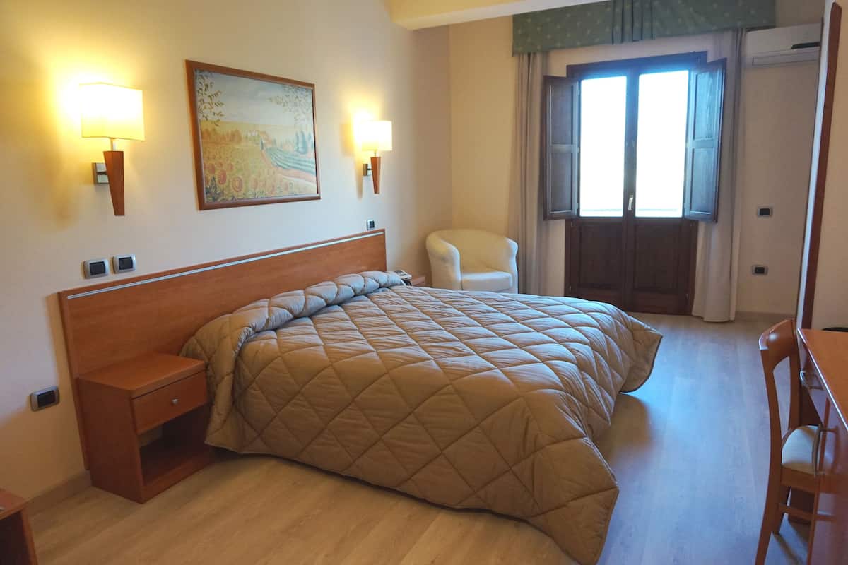 Een hotelkamer met een bed, nachtkastje, stoel en een schilderij aan de muur.