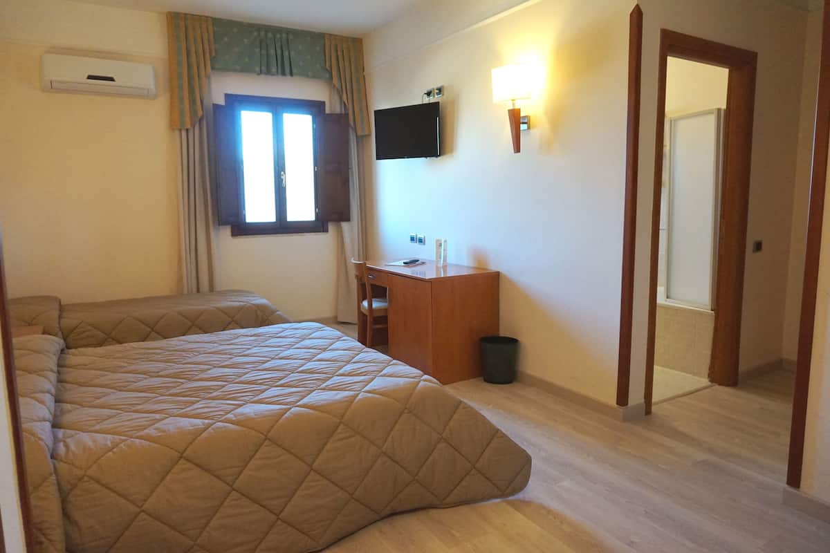 Een hotelkamer met een groot bed, een bureau met stoel, een aan de muur bevestigde televisie en een spiegel.