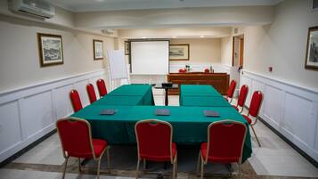Ein Konferenzraum mit einem langen Tisch, roten Stühlen, einer Projektionsleinwand und gerahmten Bildern an den Wänden.