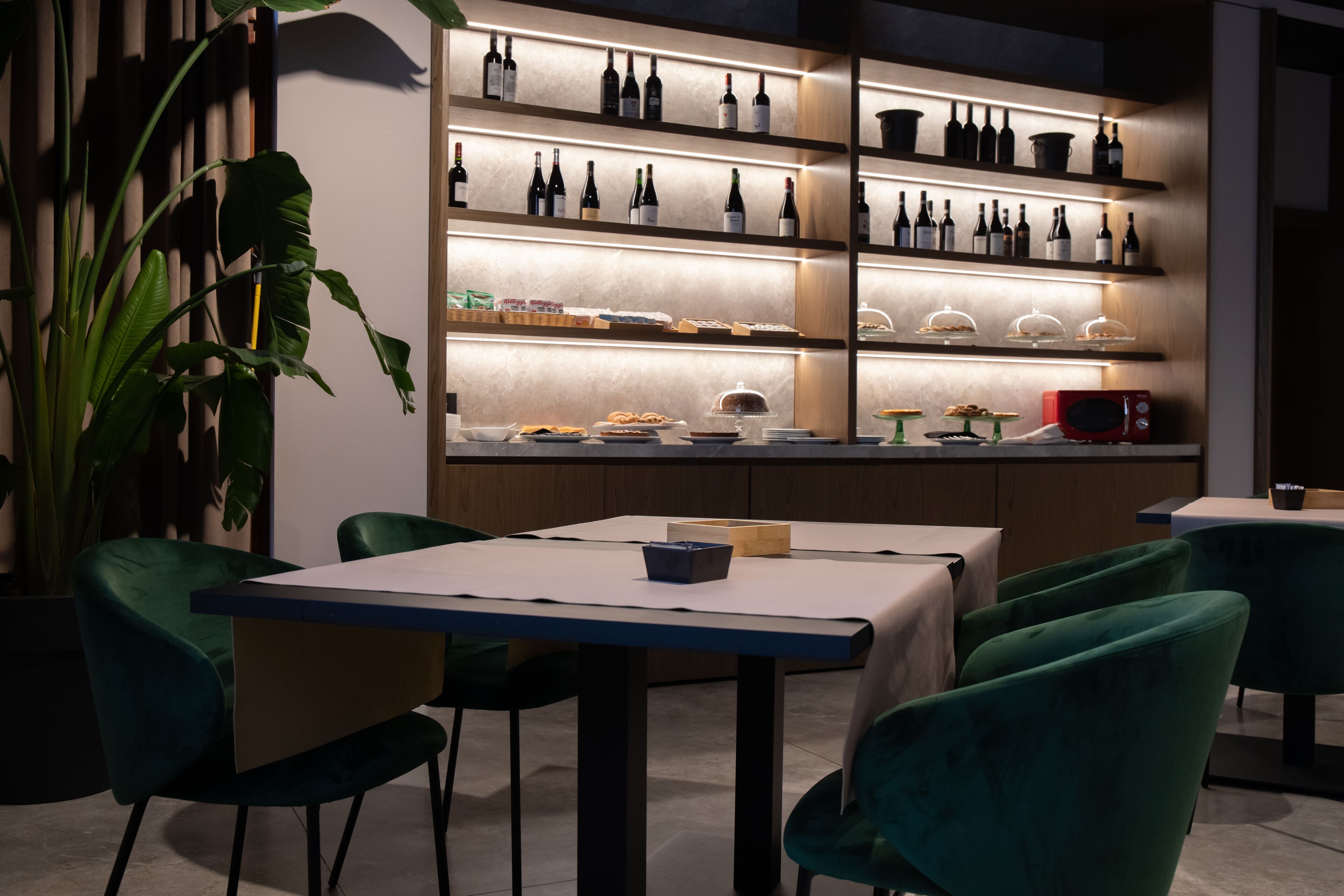 Ein Restaurant mit einer langen Theke, grünen Stühlen und Regalen voller Flaschen und Lebensmitteln.