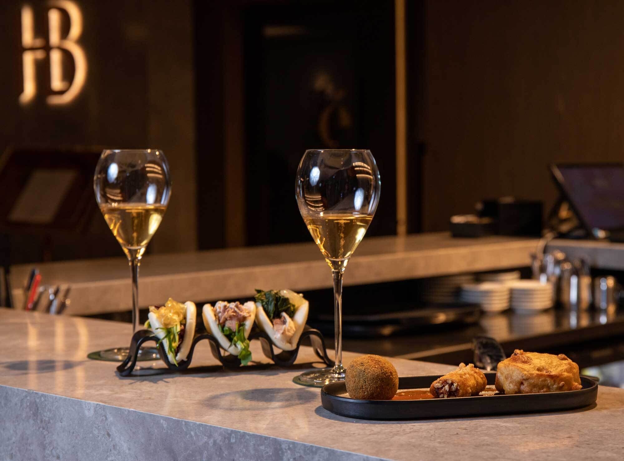 Un comptoir de restaurant avec deux verres de vin blanc, une assiette de nourriture et un ordinateur portable.