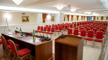 Un salón de conferencias con hileras de sillas rojas, un atril de madera y un escritorio con un teléfono y botellas.