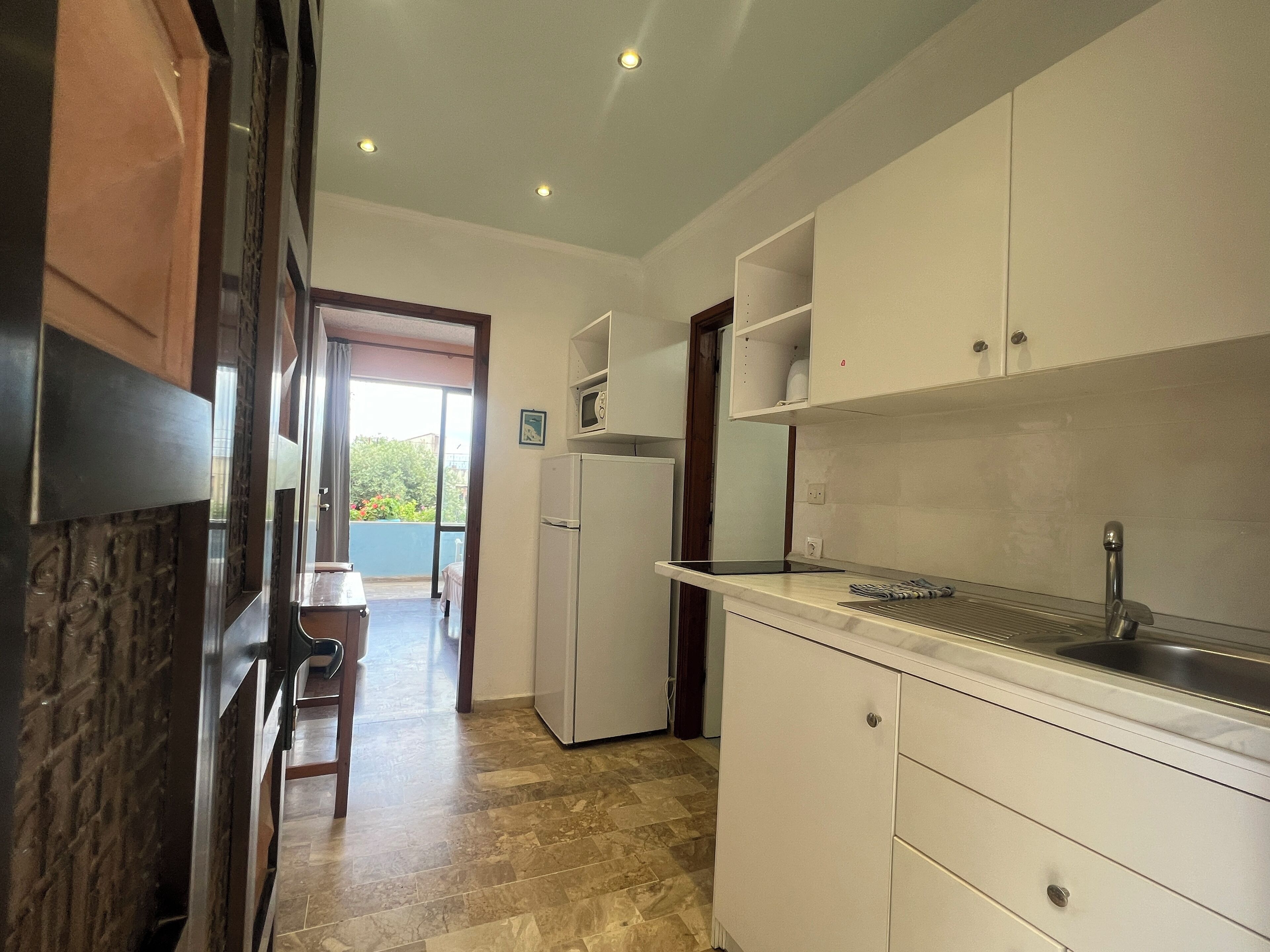 Una cocina con armarios blancos, un lavamanos de acero inoxidable y piso de baldosas.