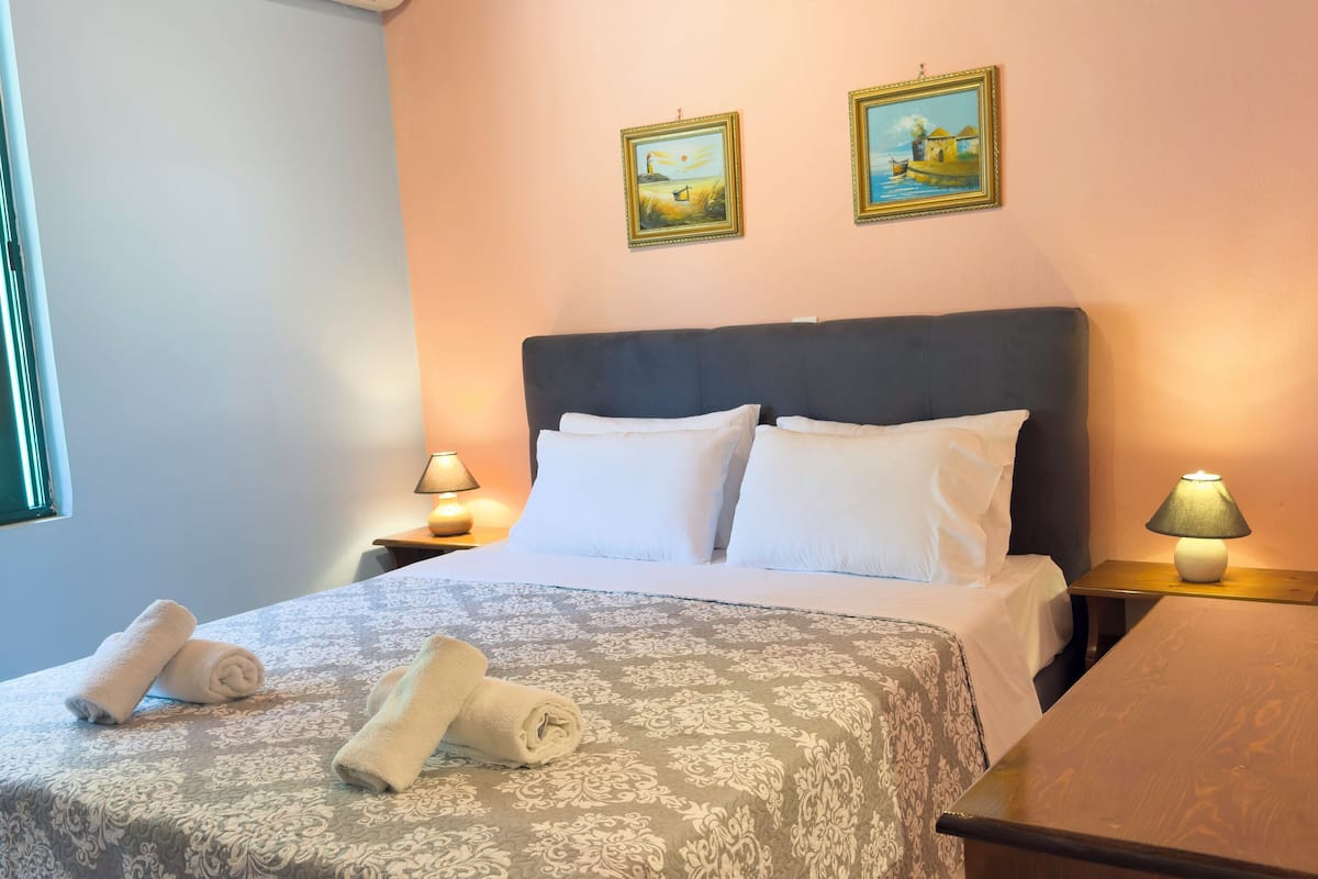 A neatly made bed with a patterned bedspread, two bedside lamps, and two framed paintings on the wall.