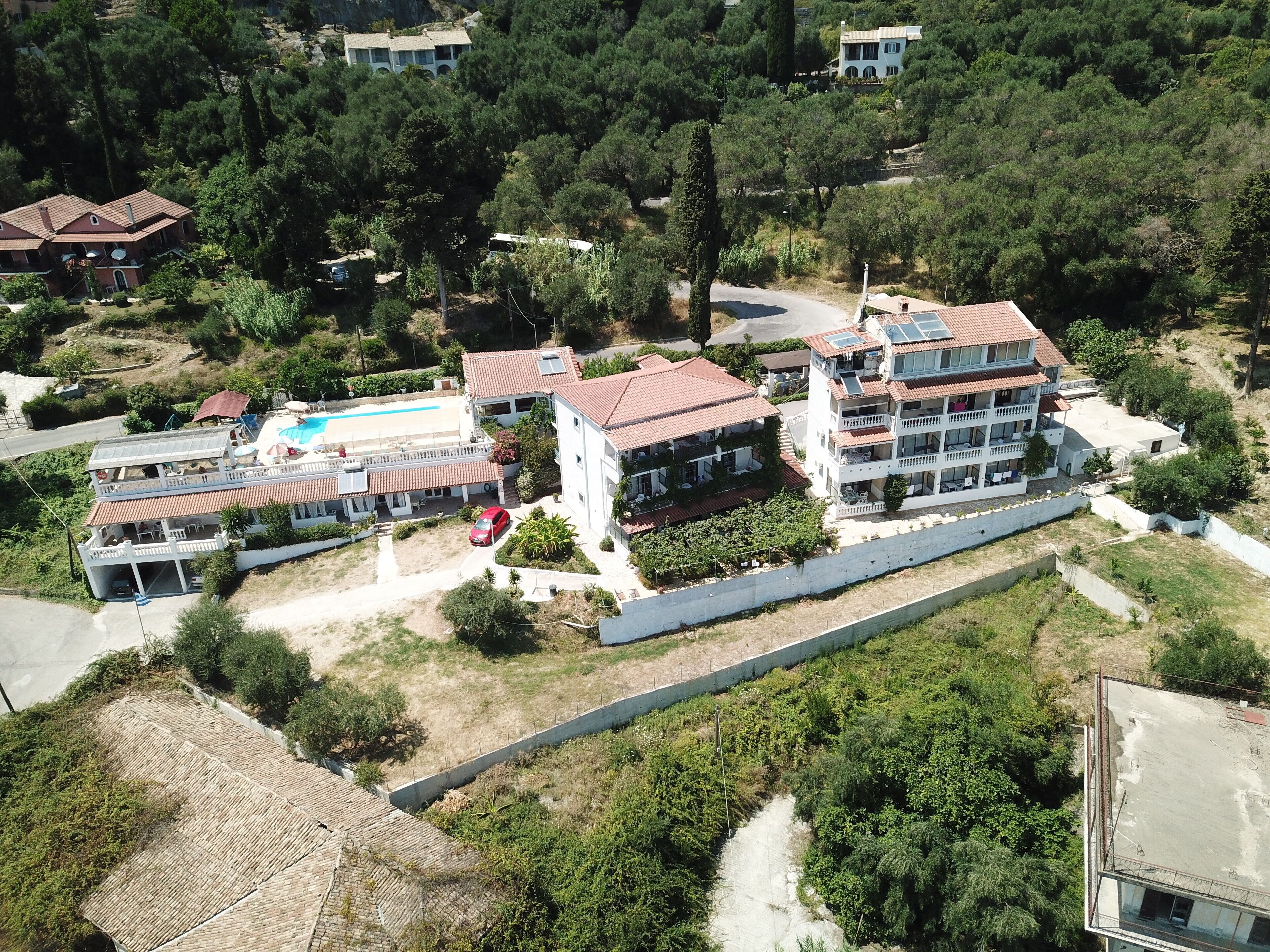 Un hotel de varios pisos con piscina, rodeado de vegetación y otros edificios.