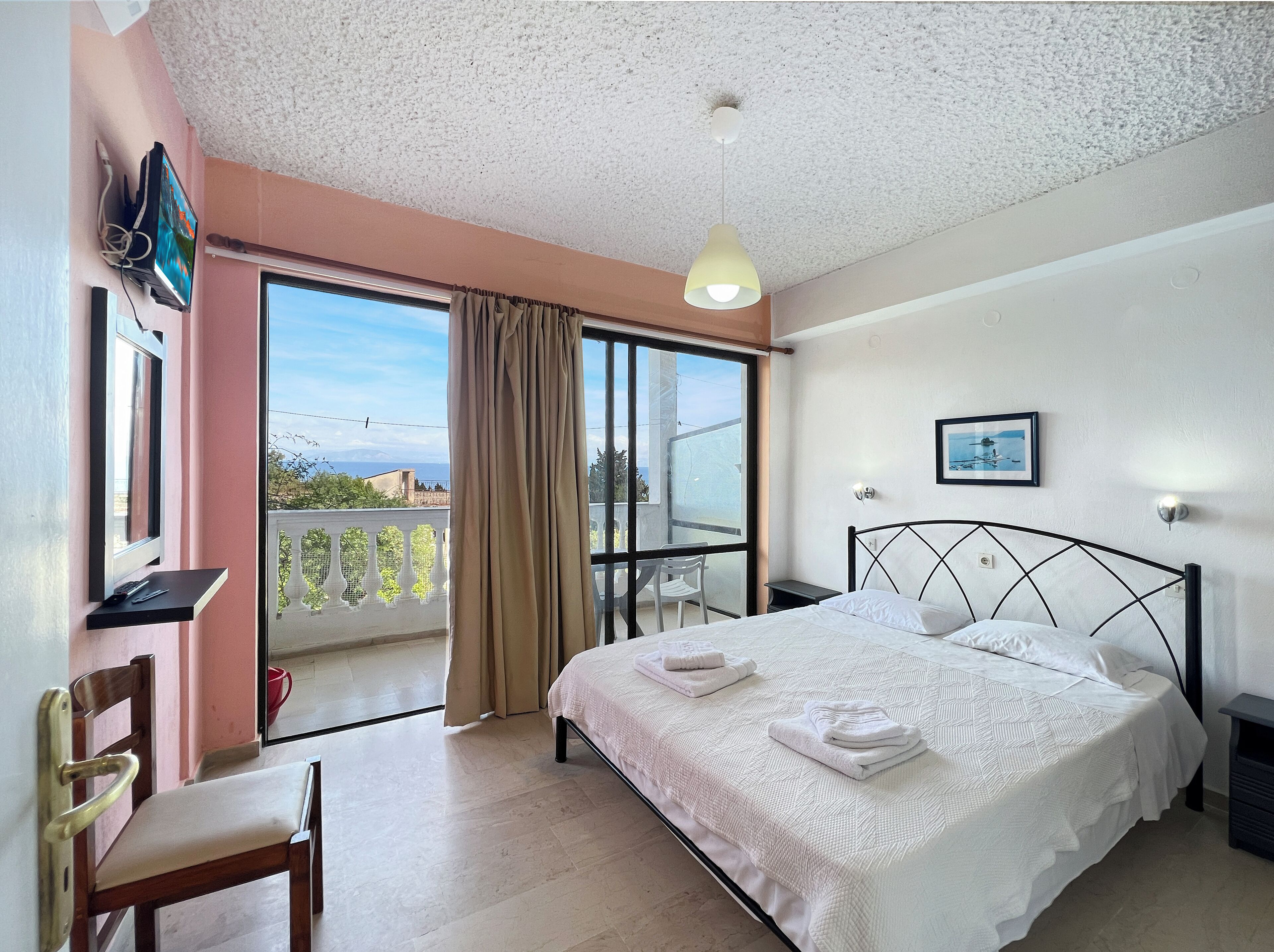 Una camera d'albergo con un letto, una scrivania, una sedia e un balcone con vista.