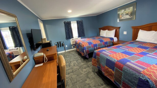 Een hotelkamer met twee bedden, een bureau, een stoel, een spiegel, een televisie en een raam met gordijnen.