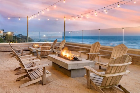 A beachside seating area with wooden chairs and a fire pit, overlooking the ocean.. Elizabeth Oceanfront Suites, an Ascend Collection Hotel