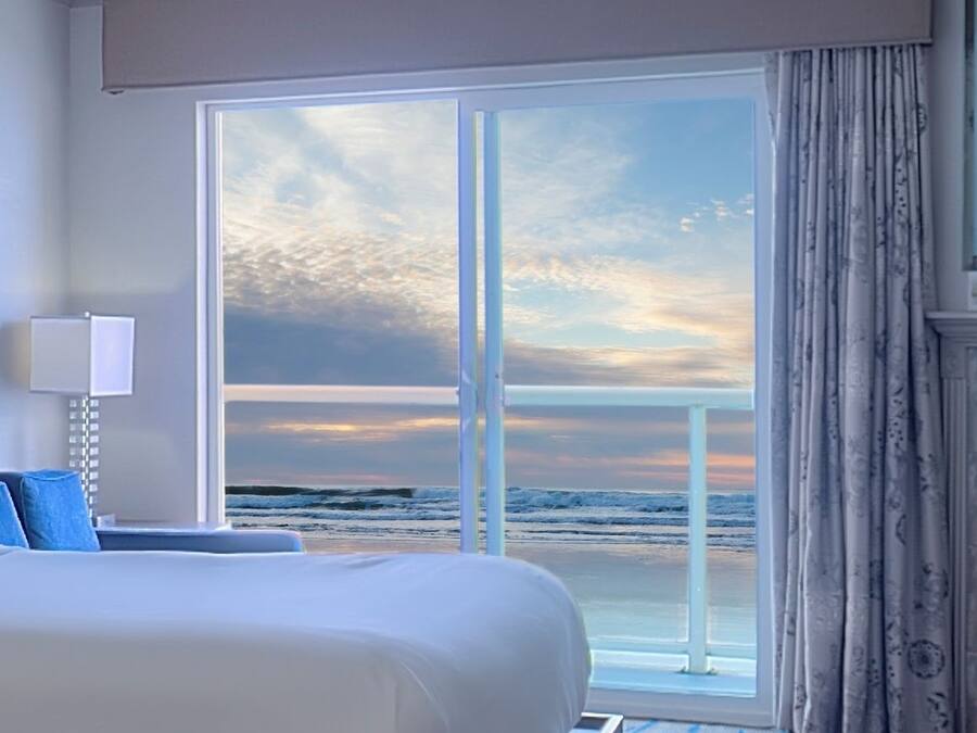 A hotel room with a large bed, a view of the ocean, and a sliding glass door.