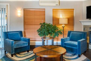 Una sala de estar con dos sillones azules, una mesa redonda de madera, una planta grande en maceta y una chimenea.