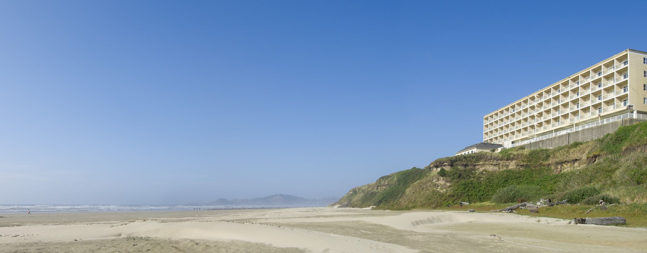 Een kusthotel met een plat dak, meerdere balkons en uitzicht op het strand en de oceaan.