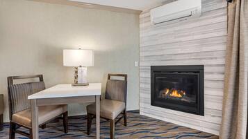 Habitación de hotel con chimenea, una mesa con dos sillas, una lámpara y una alfombra estampada.