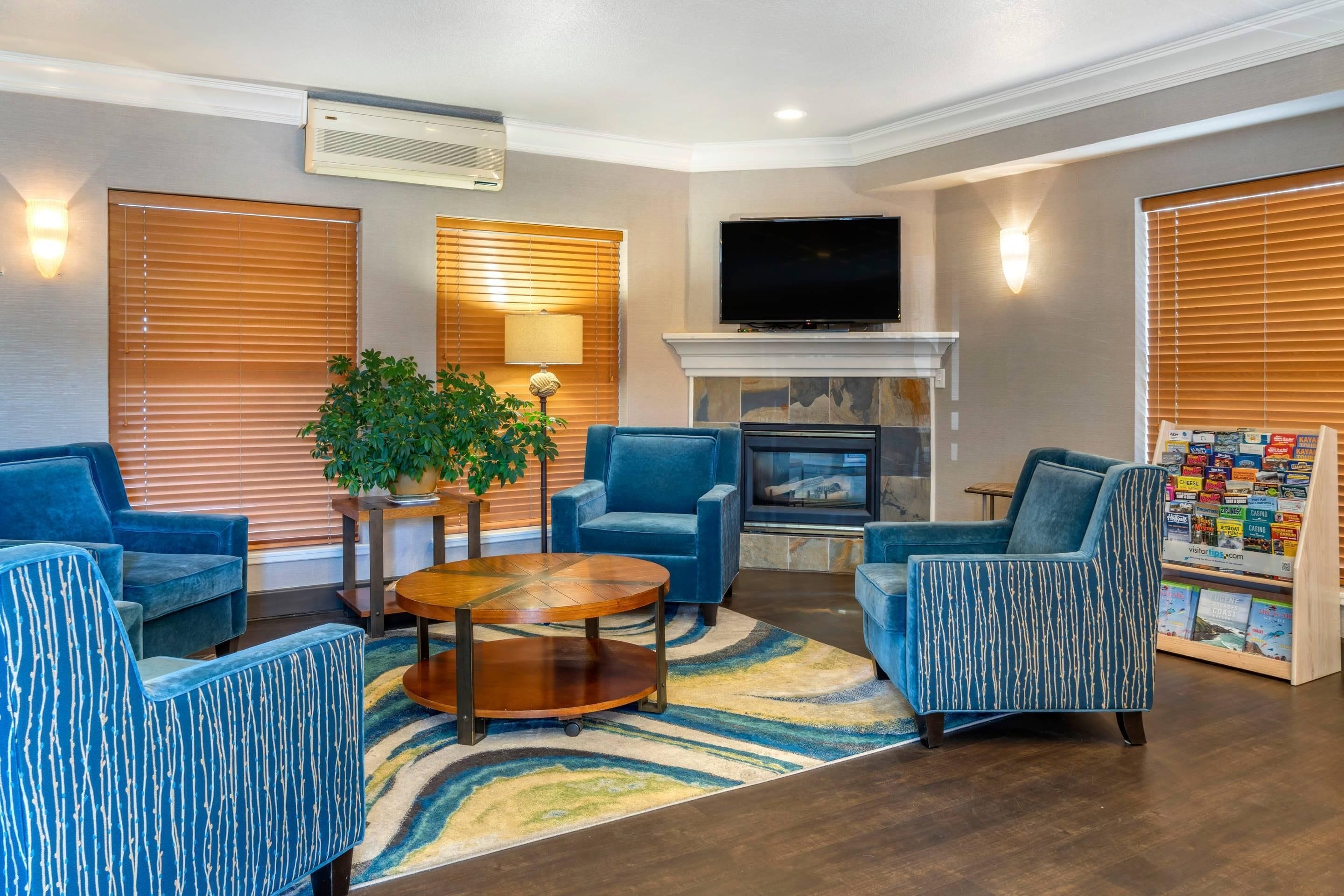A living room with blue upholstered chairs, a wooden coffee table, a fireplace, and a television mounted above it.