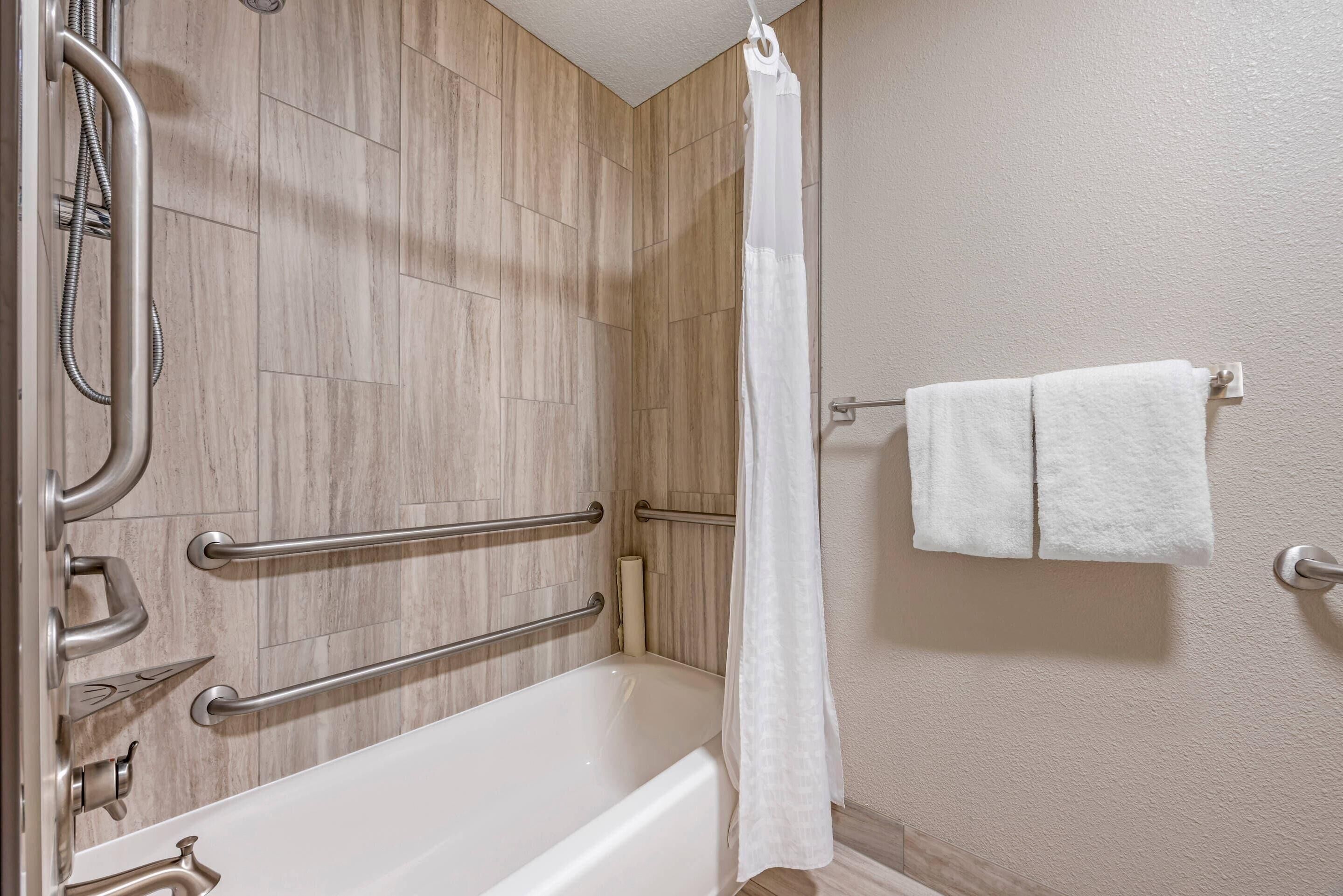 Un baño con bañera, barras de apoyo, cabezal de ducha y toallero.