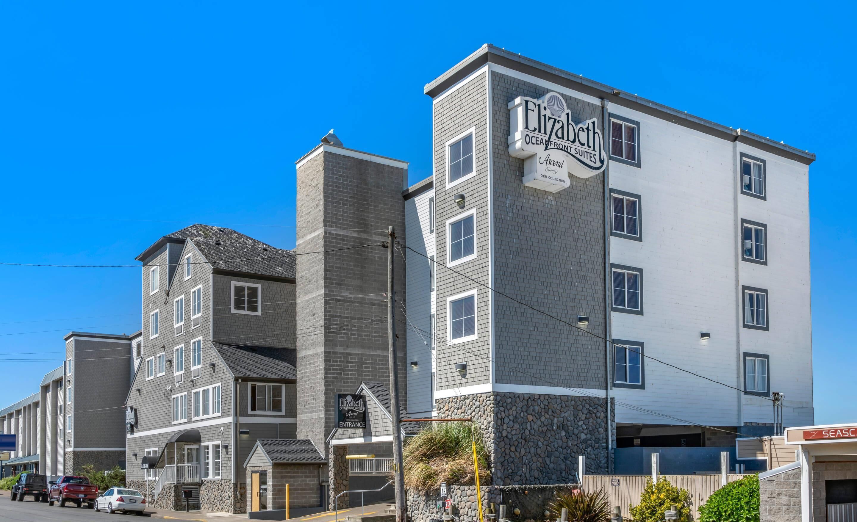 Un hotel de varios pisos con un llamativo letrero de Elizabeth Oceanfront Suites, fachada de piedra y una entrada en esquina.