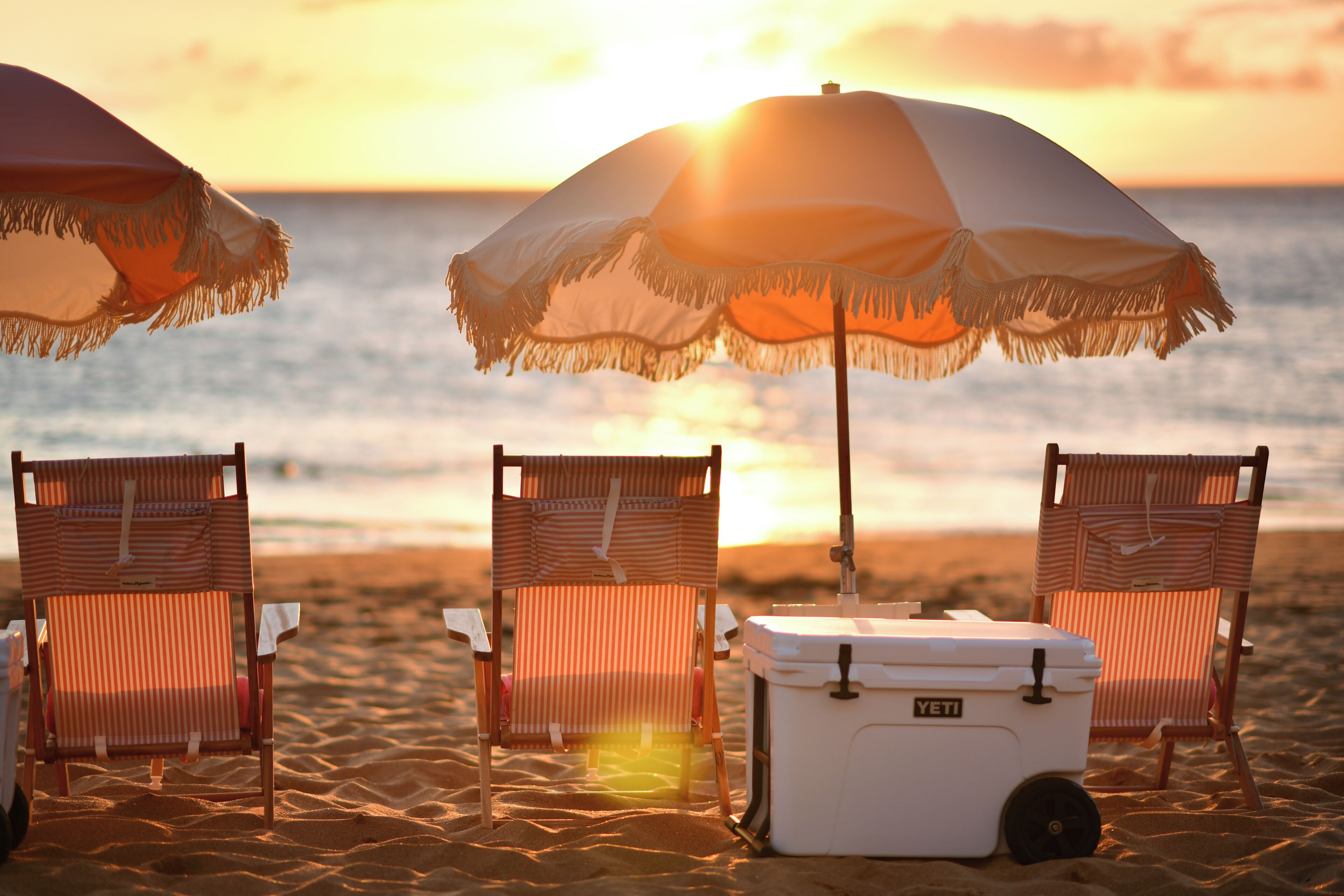 Deux chaises de plage et une glacière sur le sable, avec un coucher de soleil en arrière-plan.