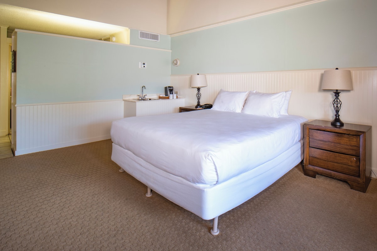 Un dormitorio ordenado con una cama grande, mesitas de noche y un aparador.