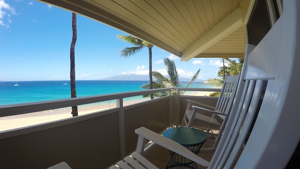 A balcony with white chairs and a small table, overlooking a beach with palm trees and the ocean. - Kaanapali Ocean Inn (Lahaina)