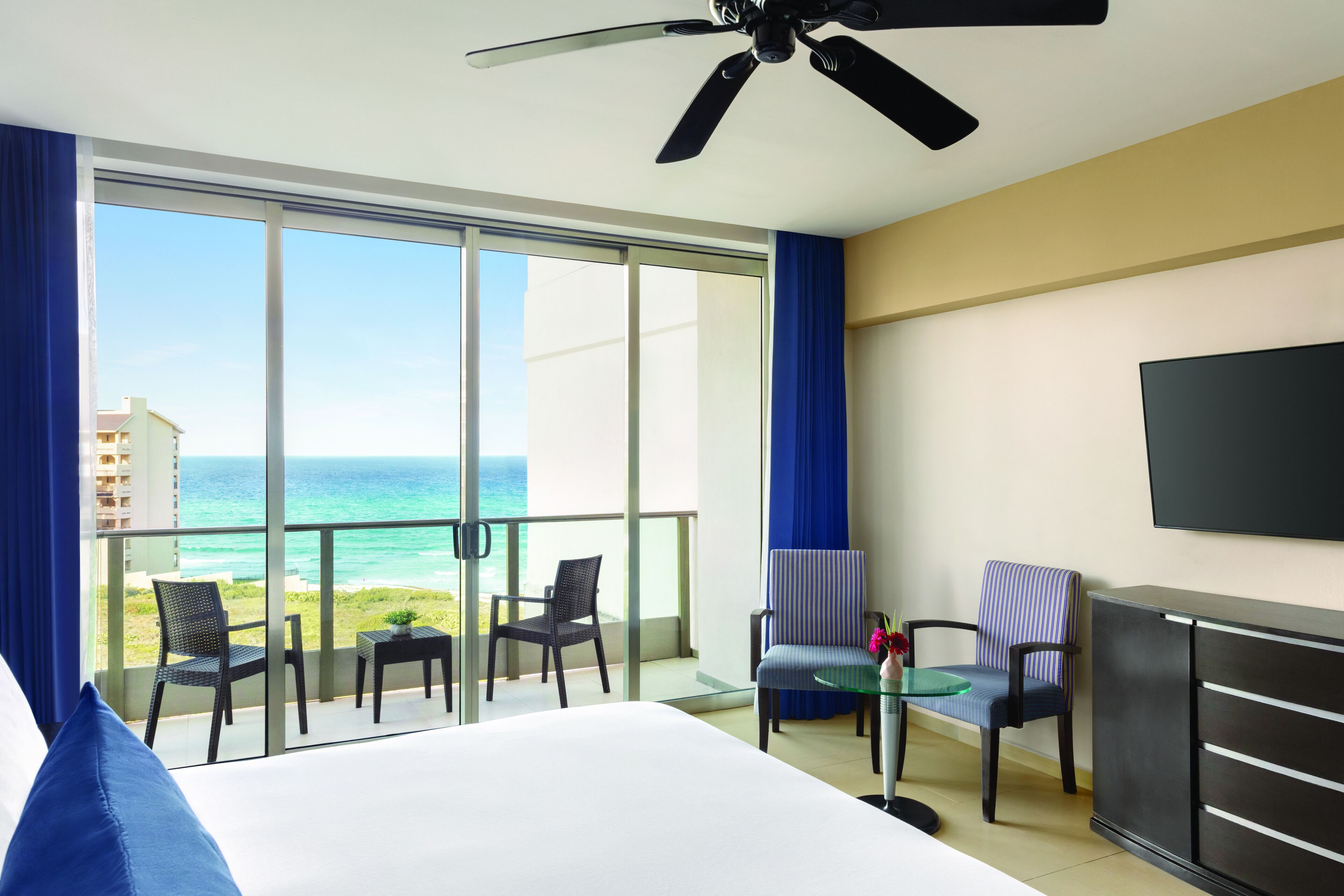 Ein Hotelzimmer mit Balkon, Bett, Fernseher und Deckenventilator.