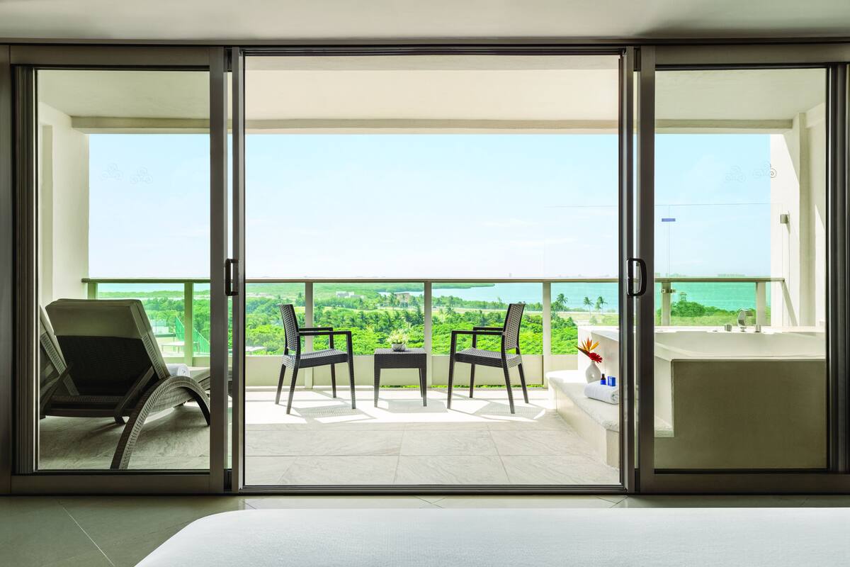 A balcony with a view of the sea, two chairs, a small table, and a bathtub.