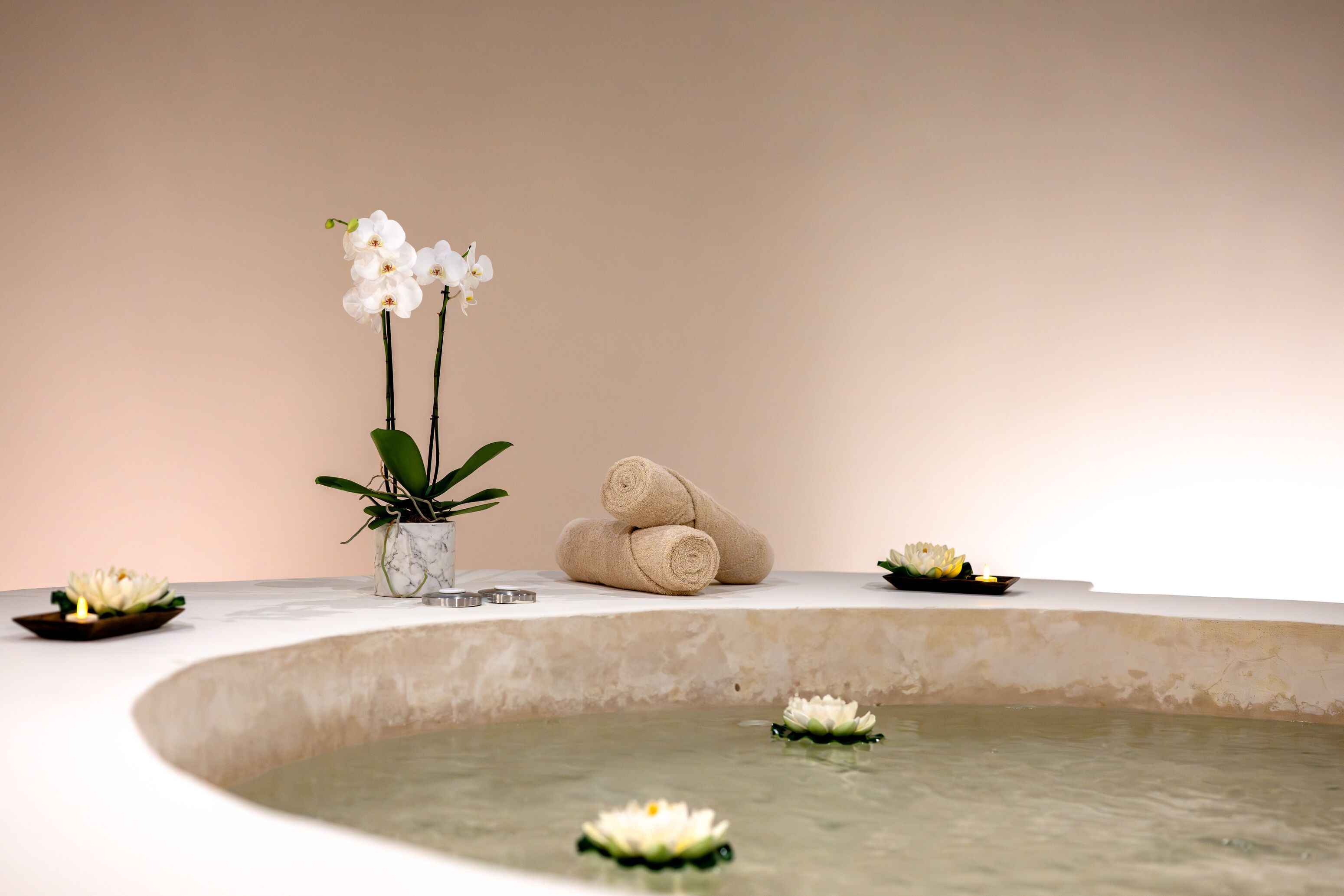 A spa area with a marble pool, white orchids, and rolled towels.