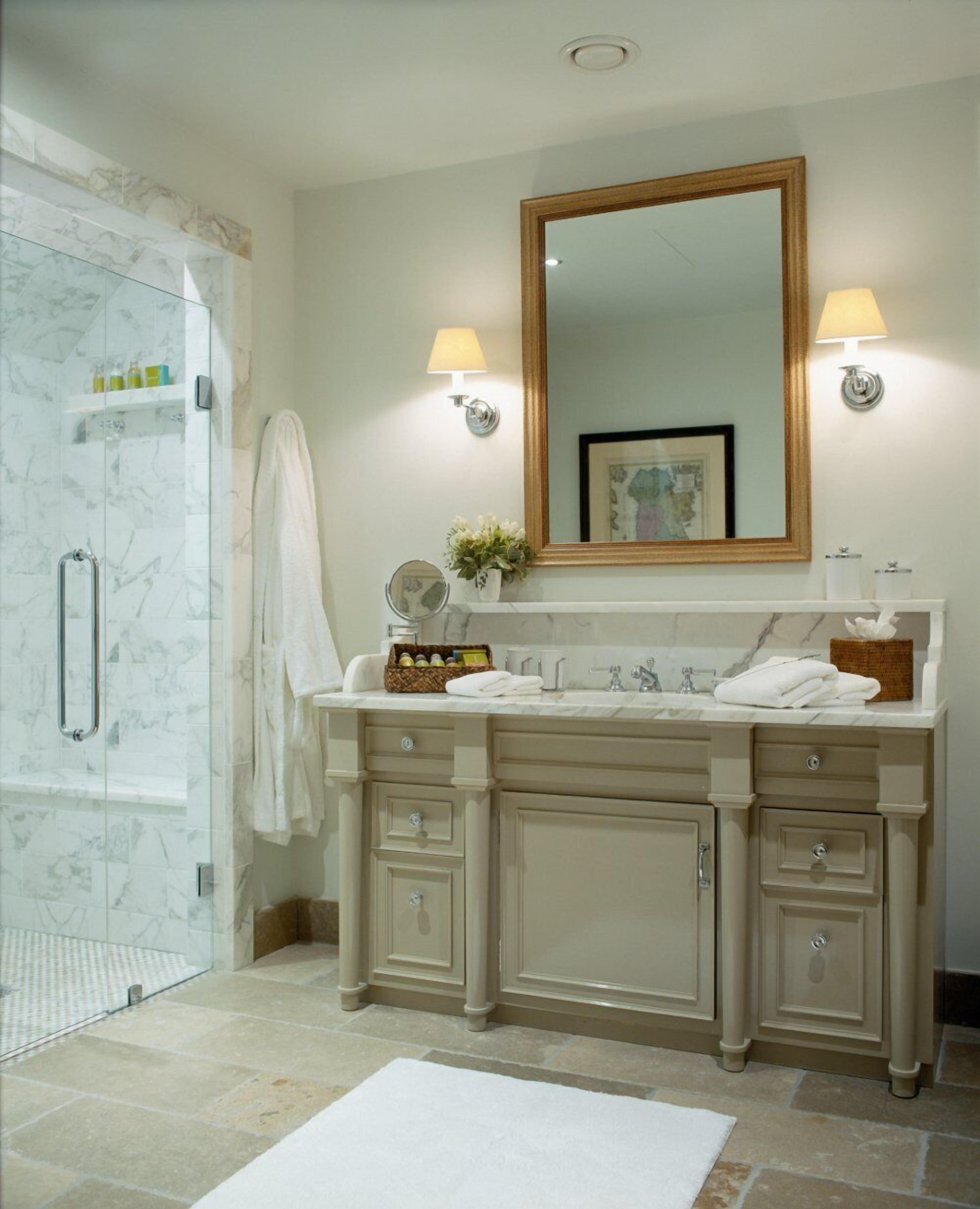 A bathroom with a marble shower, a vanity with a large mirror, and two wall-mounted lights.