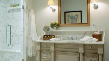 A bathroom with a marble shower, a vanity with a large mirror, and two wall-mounted lights.