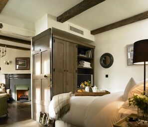 A bedroom with a bed, a wooden wardrobe, a fireplace, a television, and a tray with breakfast items.