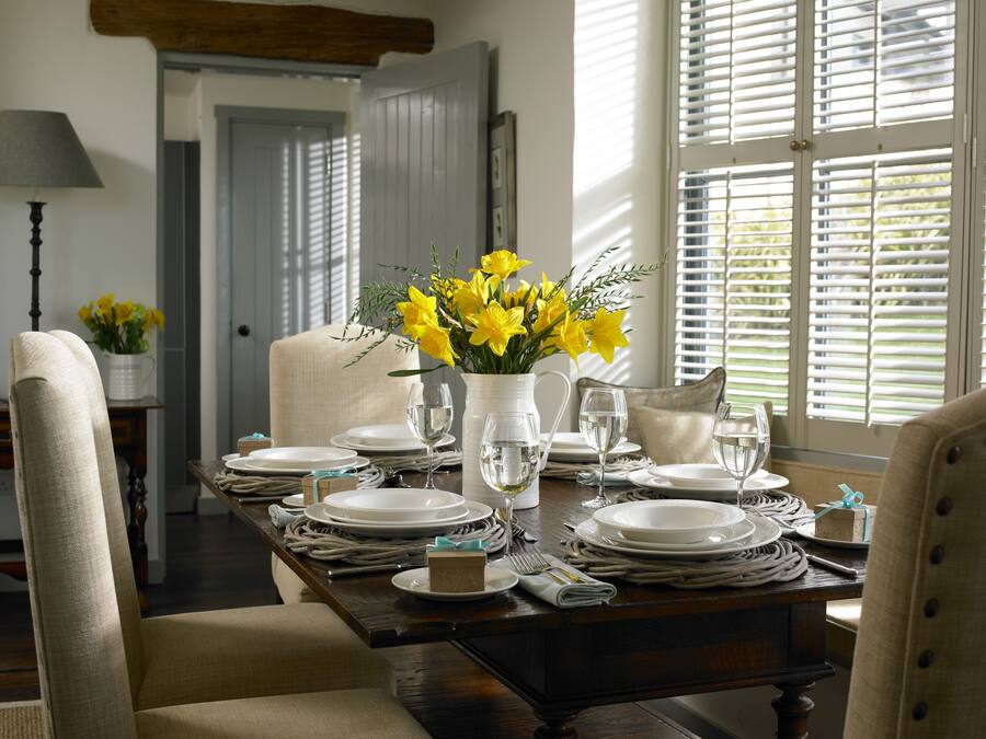 A dining table set with white plates, glasses, and a vase of yellow flowers.