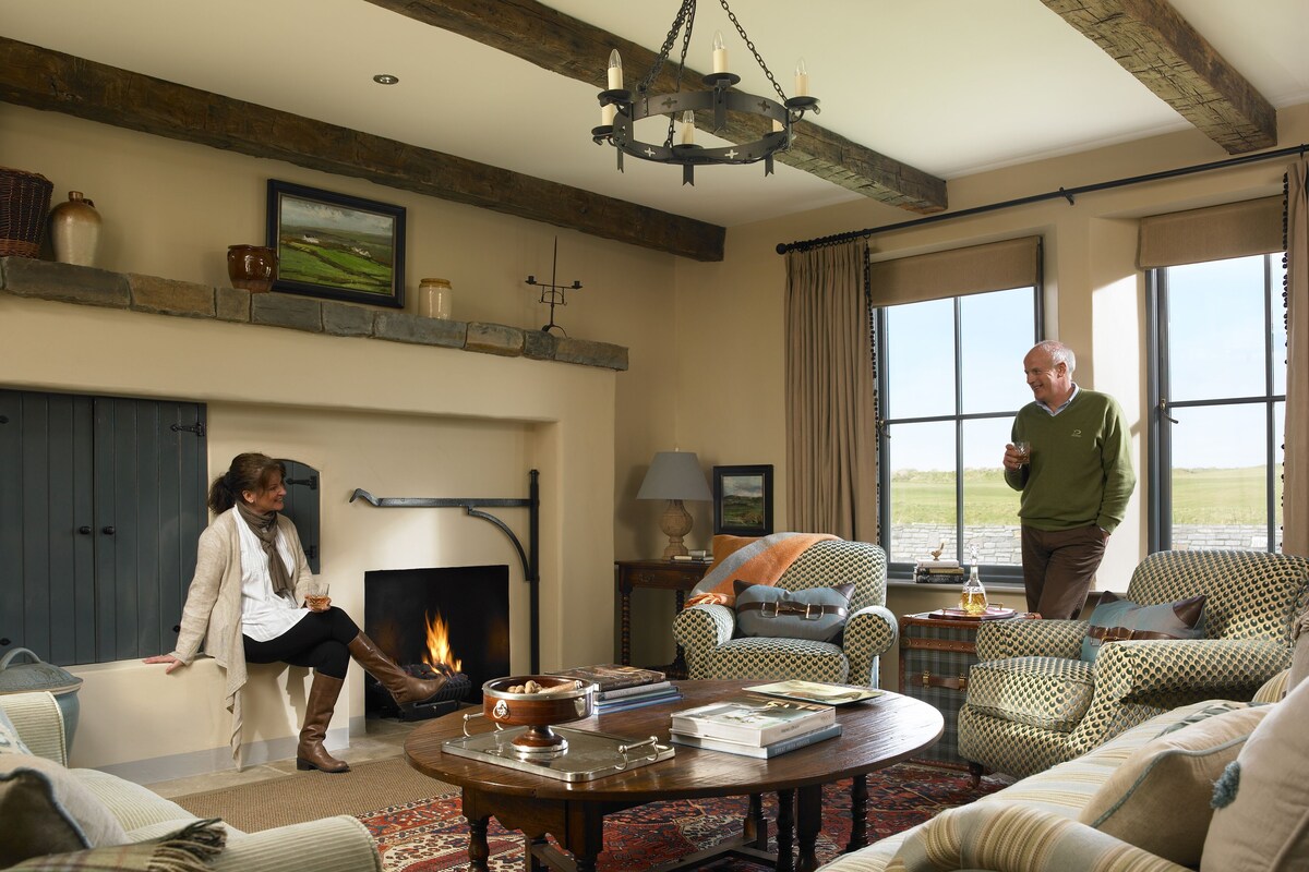 A cozy living room with a fireplace, comfortable seating, and a view of the outdoors.