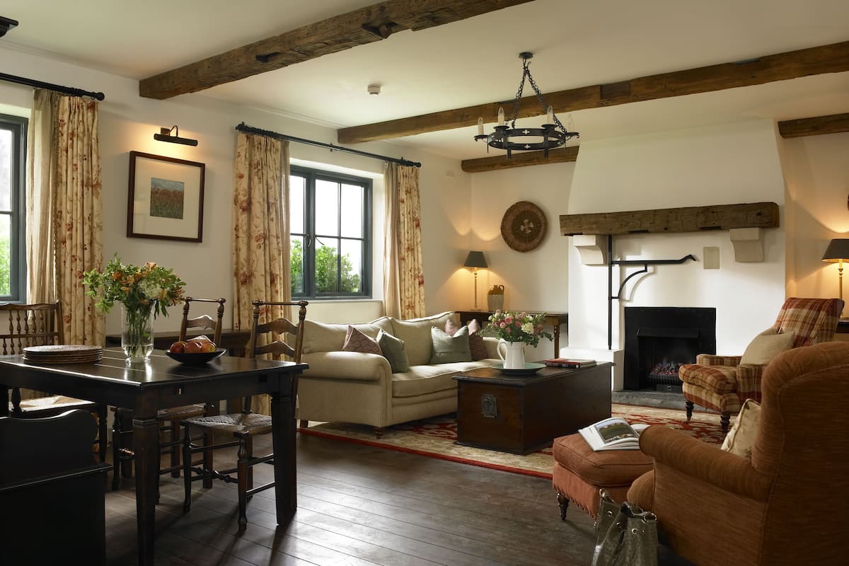 A cozy living room with a fireplace, wooden beams, a dining table with chairs, and a sofa.