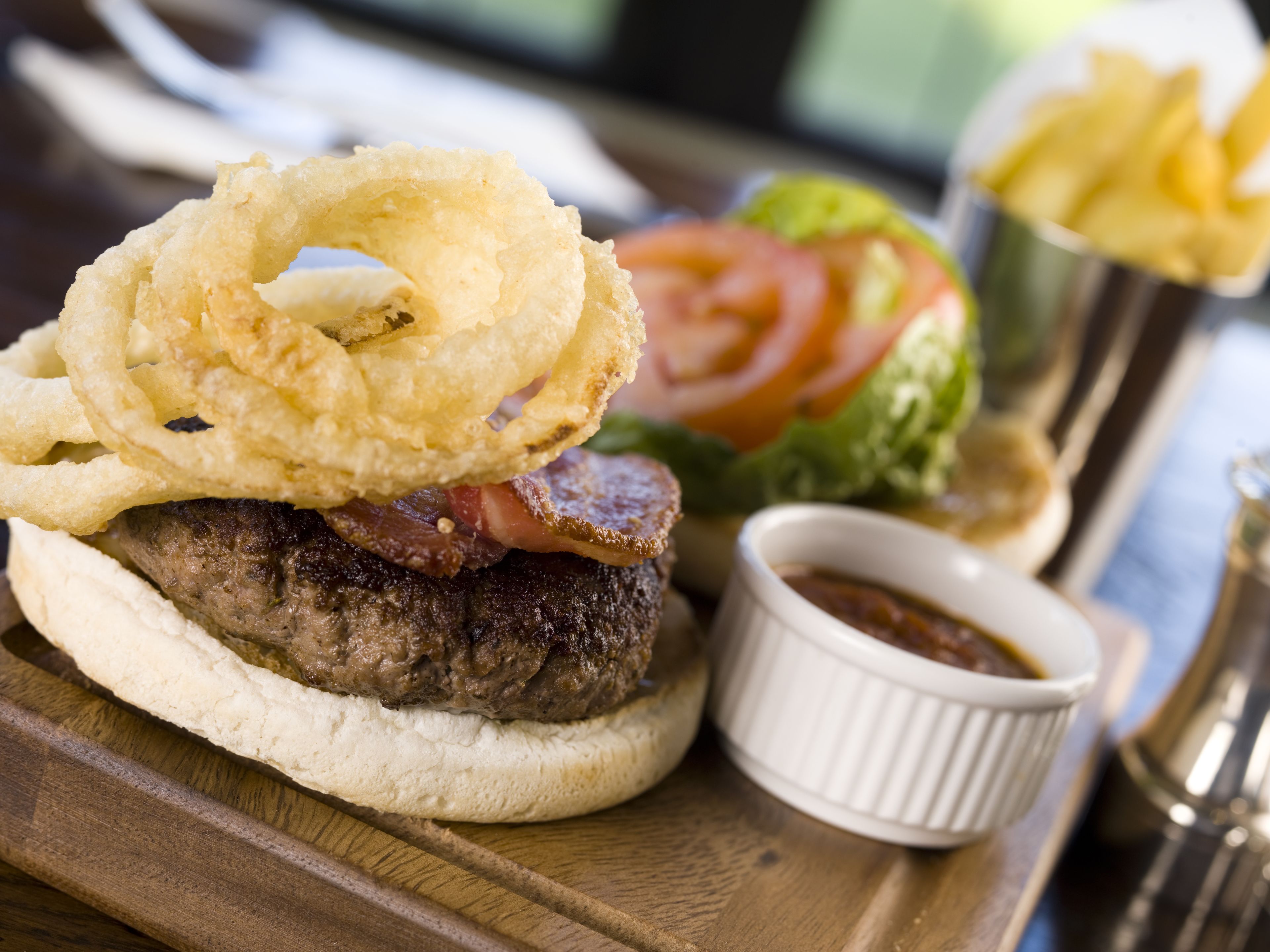 Ein Burger mit Zwiebelringen, einem kleinen Salat und Pommes auf einer Holzplanke.