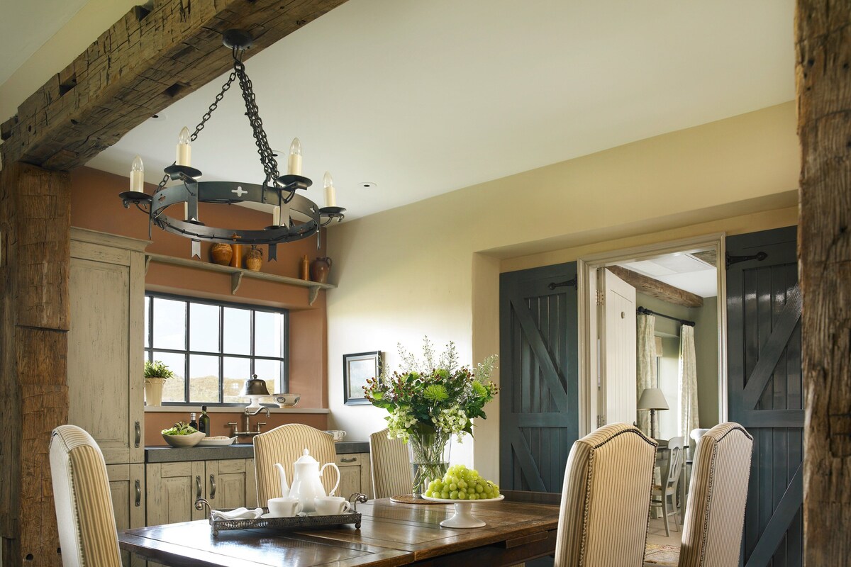 A dining area with a wooden table, striped chairs, and a chandelier. There is a window with a view of the outside, and a door with a barn-style design.
