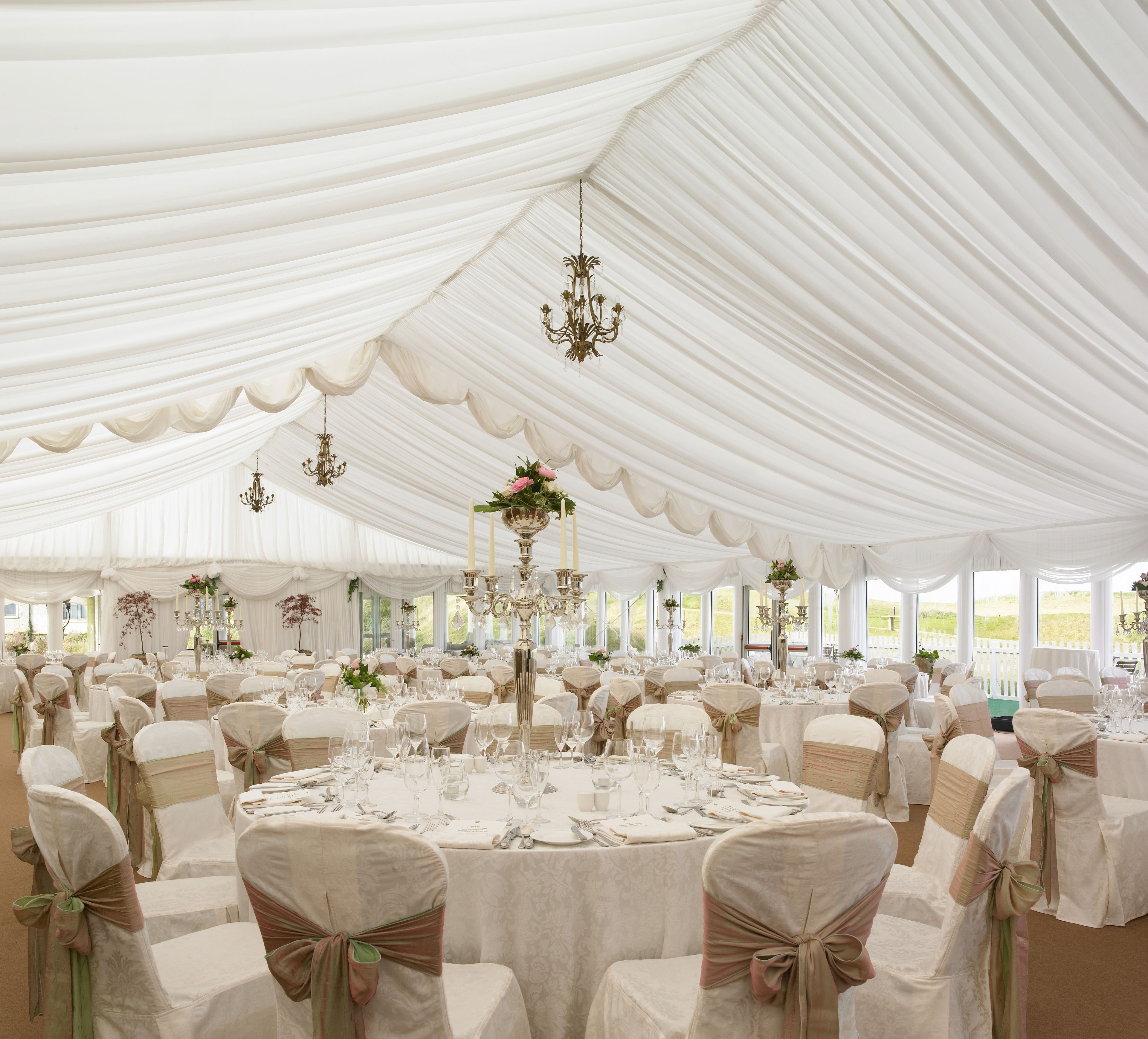A large tented event space with round tables, chairs, and chandeliers.