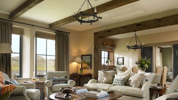 A cozy living room with a patterned sofa, a coffee table, and a large window with curtains.
