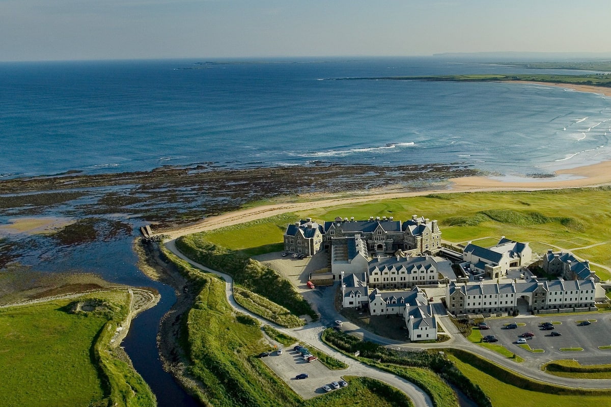 An aerial view of a large estate with a castle-like building, a beach, and a river.