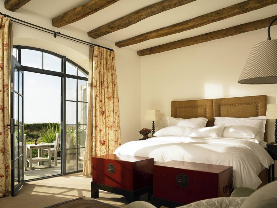A bedroom with a bed, a nightstand, a lamp, a wooden headboard, and a view through a glass door to an outdoor area.