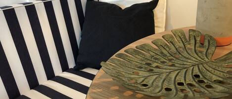A striped sofa with a black pillow, a wooden table with a decorative leaf, and a white wall.