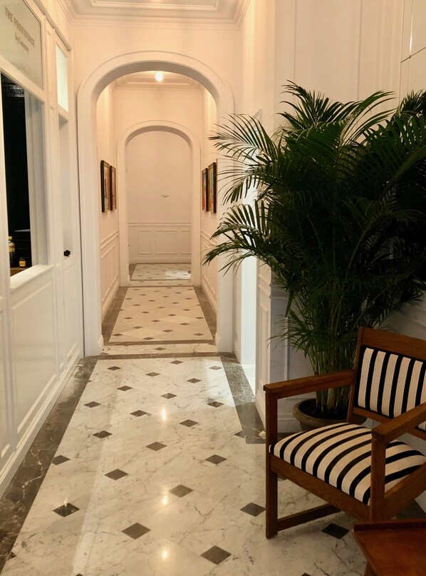 A hallway with a marble floor, a wooden chair with striped cushions, and a large potted plant. - Getaway Oostende (Ostend)