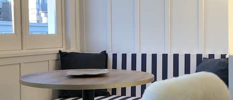 Un rincón con asientos, una mesa redonda, cojines a rayas y un sillón blanco mullido.