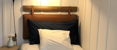 A neatly made bed with a wooden headboard, a bedside lamp, and a small table with a vase of flowers.