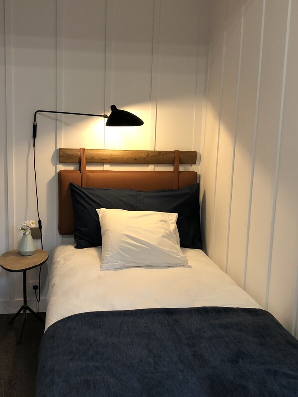A neatly made bed with a wooden headboard, a bedside lamp, and a small table with a vase of flowers. - Getaway Oostende (Ostend)