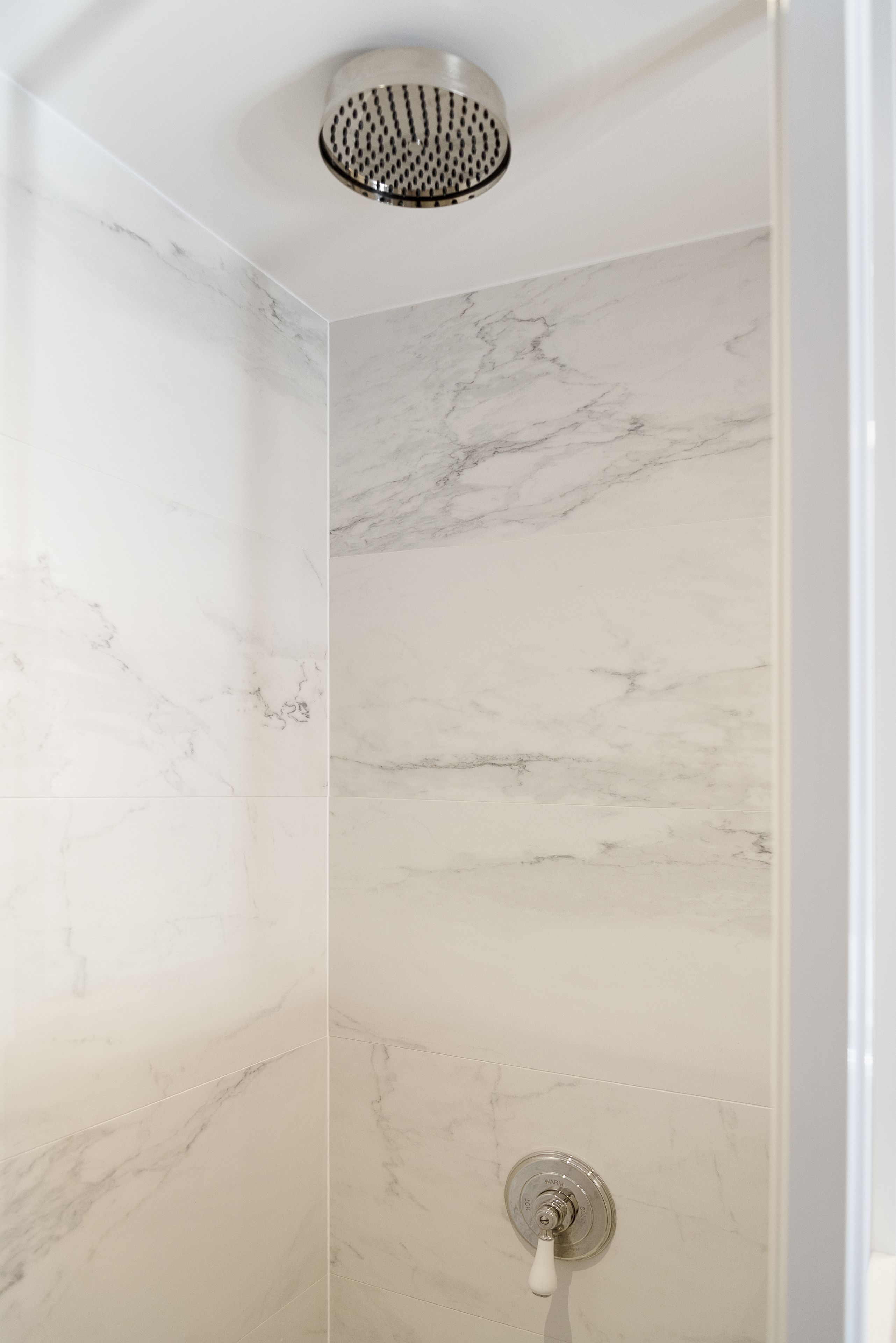 Een douche met een modern design, met marmeren wanden en een douchekop aan het plafond.