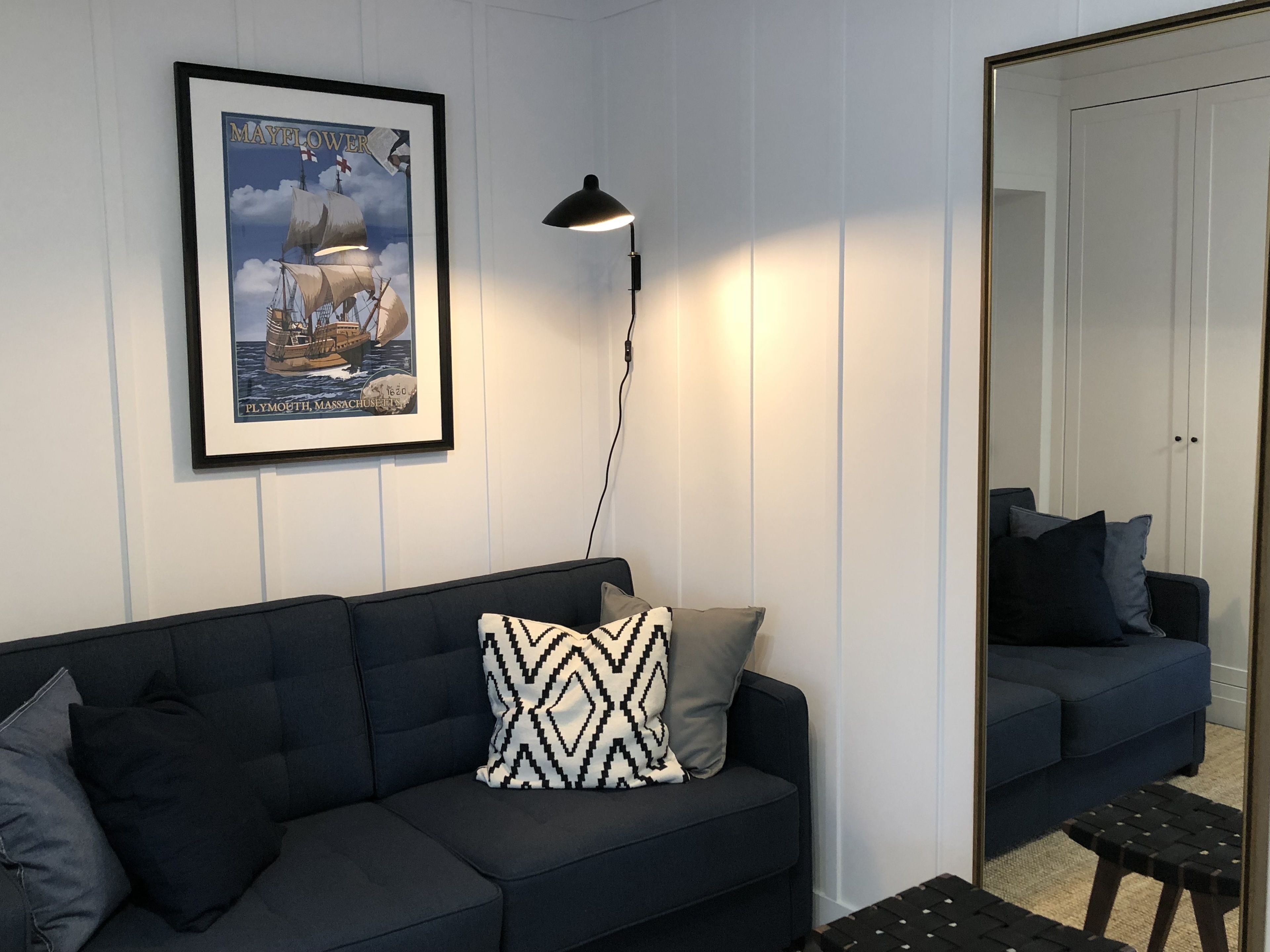 Un salon moderne avec un canapé bleu foncé, un coussin décoratif à motifs, une affiche maritime encadrée et un lampadaire.