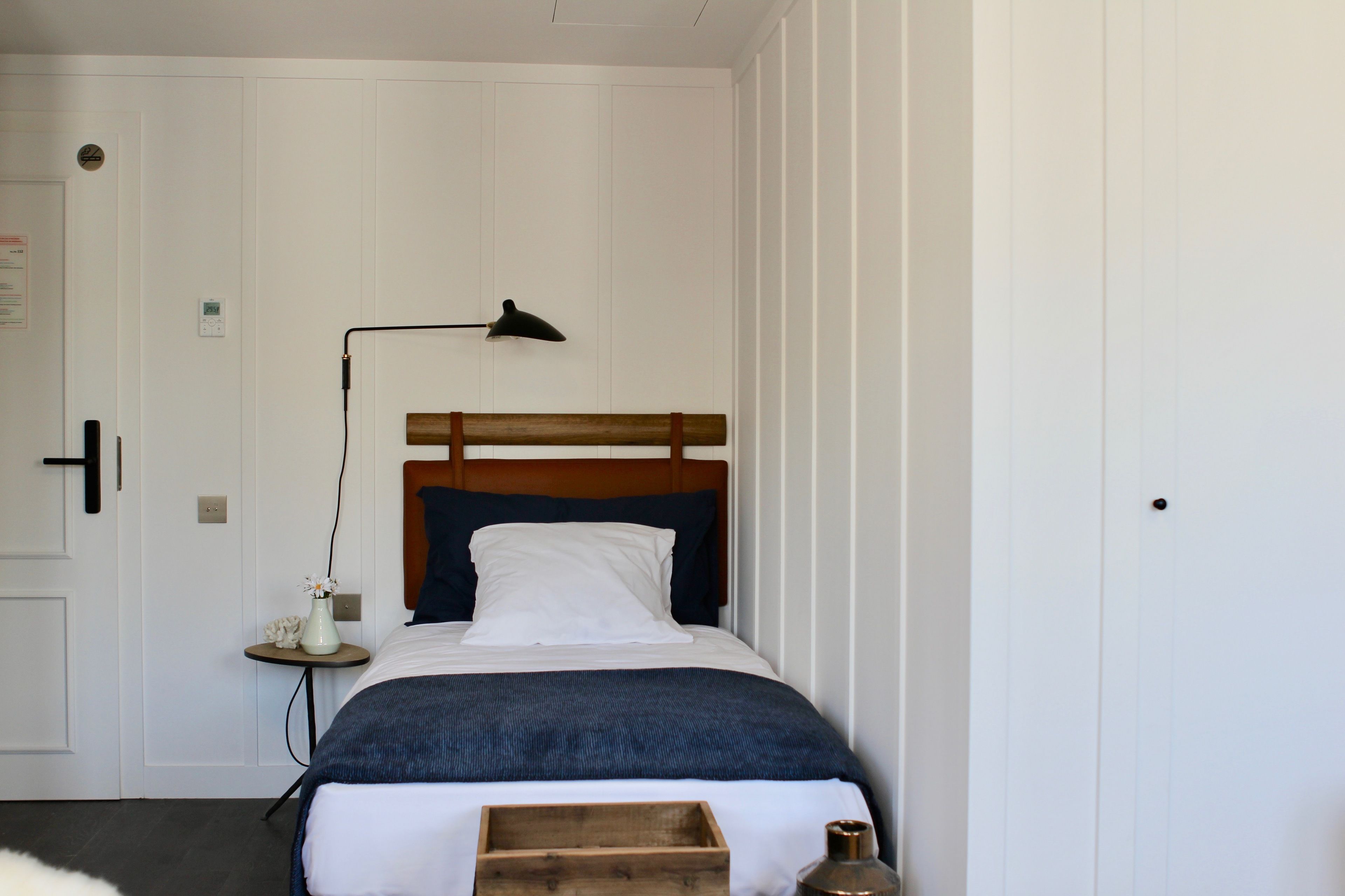 A neatly made bed with a wooden headboard, a bedside table with a lamp, and a small vase with flowers.