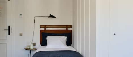 Una cama bien hecha con cabecera de madera, una mesita de noche con lámpara y un pequeño jarrón con flores.