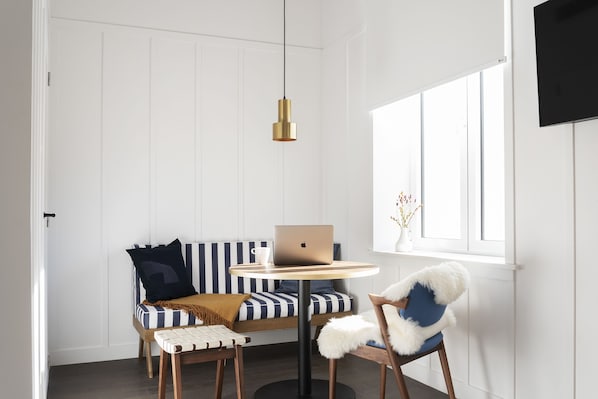 Una habitación moderna con una pared blanca de paneles, una mesa redonda con una computadora portátil, un sofá a rayas y una silla con un cojín mullido.